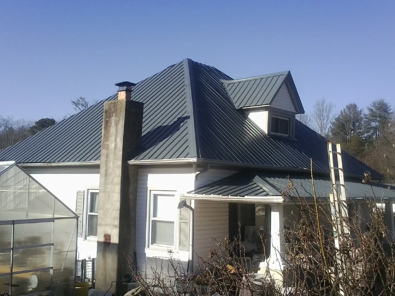 Dark blue standing seam metal roof on a white farmhouse with dormer — Slate & Tile Roof Repair by Roofing Brothers in Muskegon