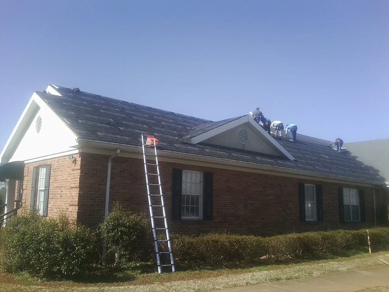 Crew tearing shingles off a brick ranch roof with a ladder set — Emergency Roof Repair work by our crew in Muskegon
