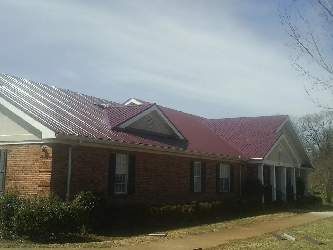 Red metal roof with gabled entries on a long brick building, from a Hail Damage Roof Repair job in Muskegon