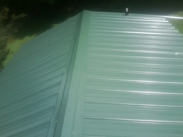 New green metal panels meeting at the ridge of a roof — Flat Roof Repair work by our crew in Muskegon