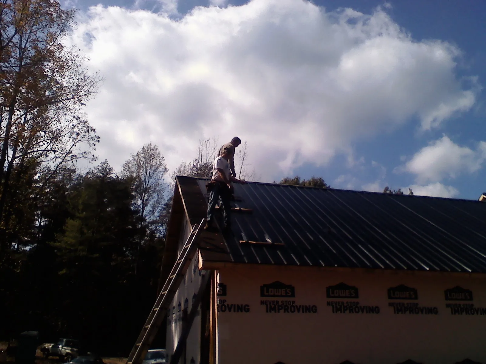 Roofer fastening dark metal panels high against a cloudy sky, from a Roof Inspection job in Muskegon