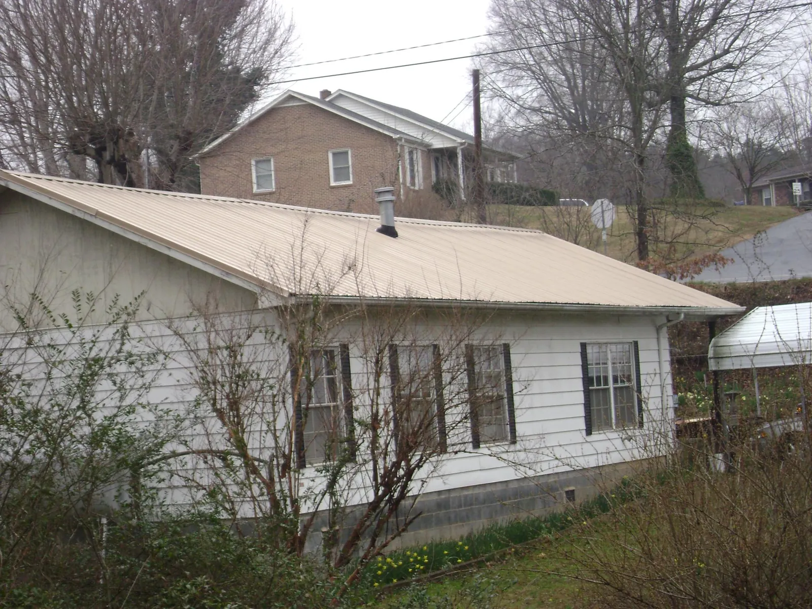 Tan metal roof on a white sided house set into a hillside — Commercial Roofing by Roofing Brothers in Muskegon