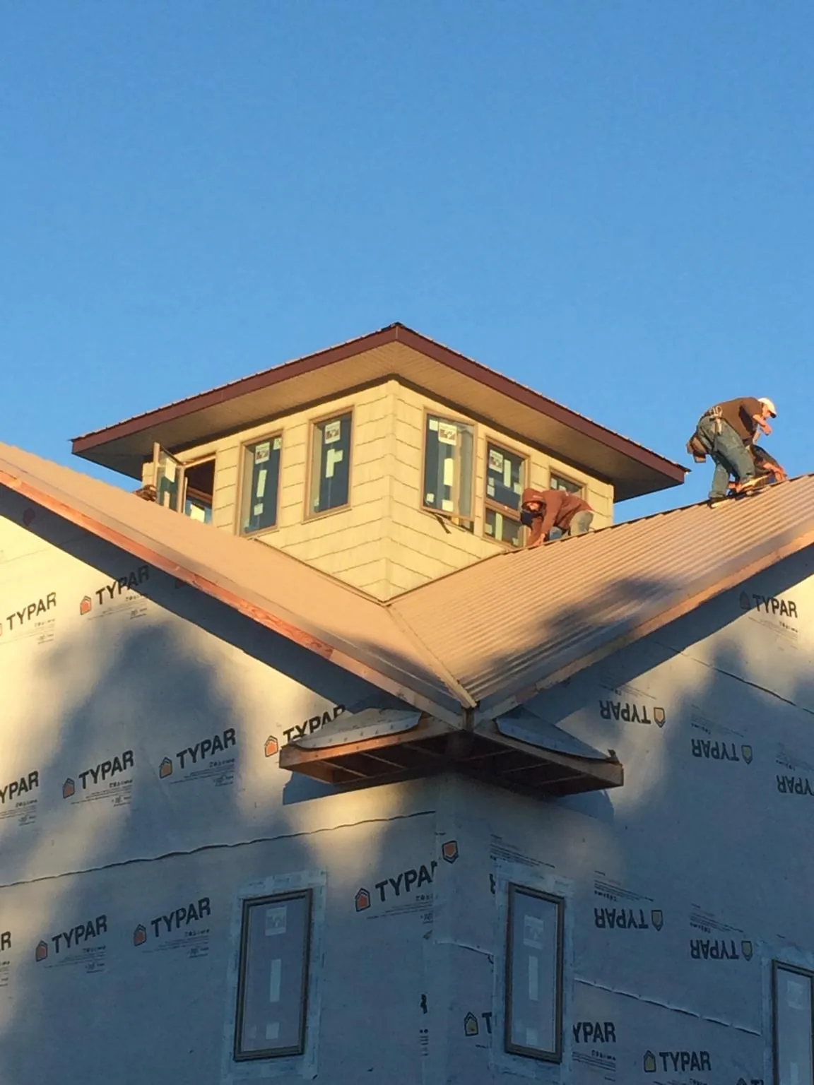 Roofers working around a rooftop cupola on a new metal roof at sunset — Roof Waterproofing in Muskegon by Roofing Brothers
